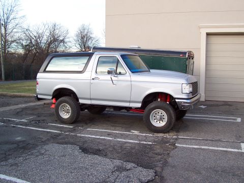 1990 Ford Bronco - This lifted Ford Bronco is parked next to a trailer in a parking lot.