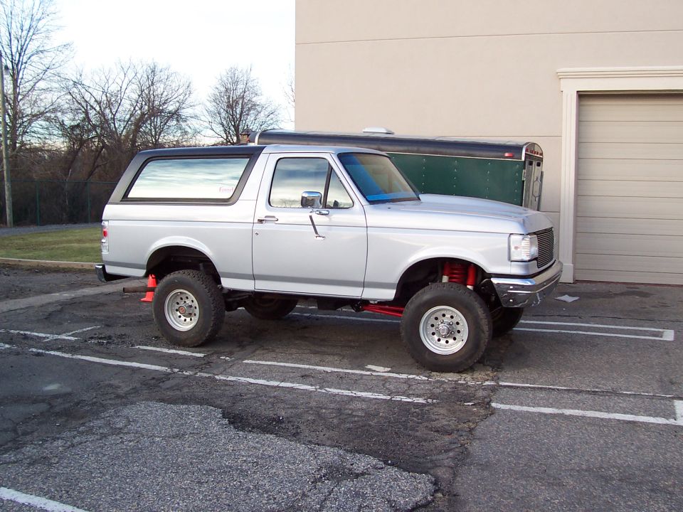 Silver lifted Ford Bronco parked in a lot, with a green trailer behind it