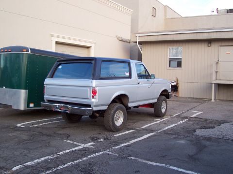 1990 Ford Bronco - This 1990 Ford Bronco is silver with a black top and is parked next to a green trailer.