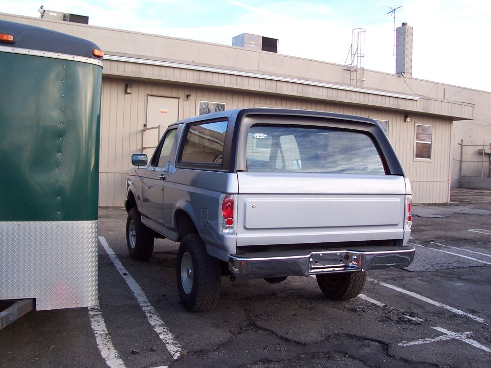 Rear view of a silver 1990 Ford Bronco parked next to a green trailer