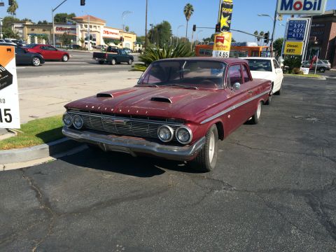 1968 Ford Mustang - A maroon sedan with distinctive hood scoops is parked near a gas station.