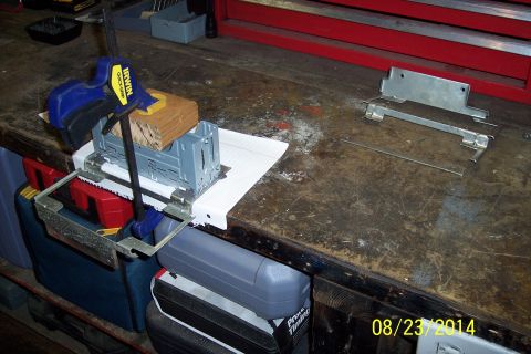 1978 Ford Bronco - Metal parts and tools on a workbench, including a bracket and a housing secured with a clamp.