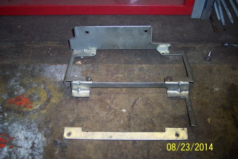 1978 Ford Bronco - A metal bracket assembly and a separate metal strip are laid out on a workbench surface.