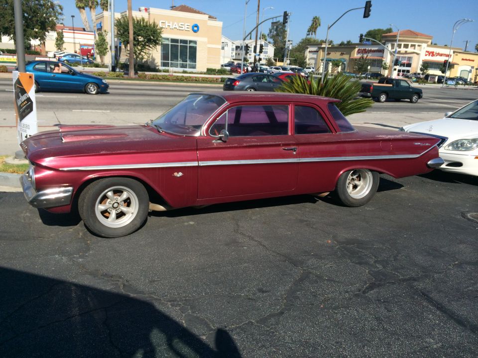 Maroon 1961 Chevrolet Biscayne sedan parked on asphalt, side view. Chrome trim, custom wheels