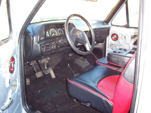1990 Ford Bronco - The interior of a truck features a dashboard with gauges, a steering wheel, and custom two-tone seats with red accents.
