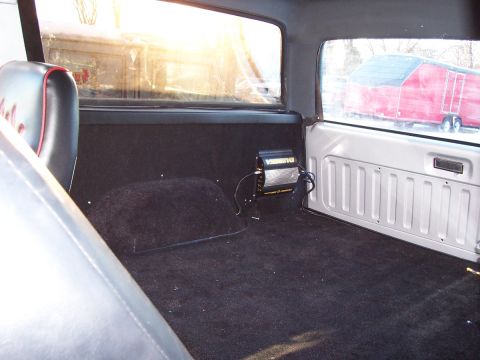 1990 Ford Bronco - The interior of a 1990 Ford Bronco shows black carpet and seats, with an amplifier mounted on the side panel.