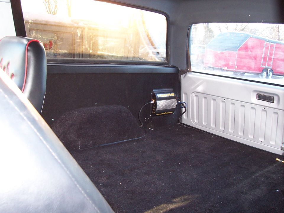 Interior of a 1990 Ford Bronco, black carpet, black seats with red trim, amplifier mounted on the wall