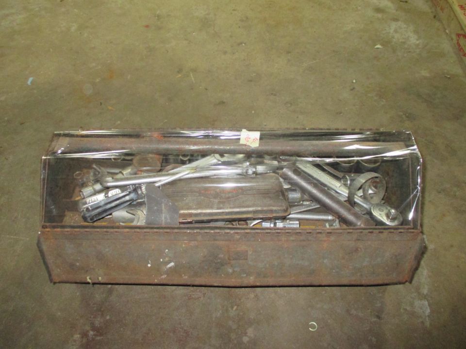 Rusty toolbox filled with various wrenches and sockets, covered in plastic wrap