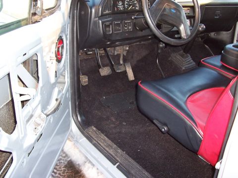 1990 Ford Bronco - The interior of a 1990 Ford Bronco shows its distinctive black and red seats, manual transmission, and exposed door panel.