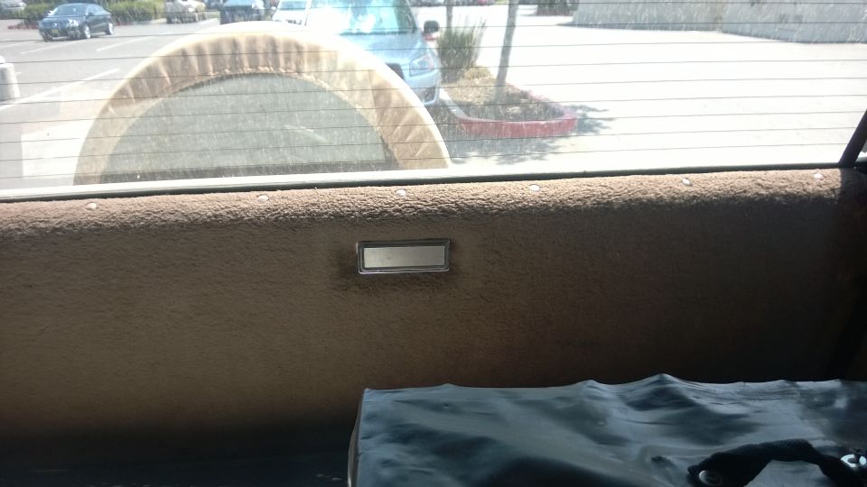 Interior rear panel with spare tire cover visible through window. Other vehicles seen outside