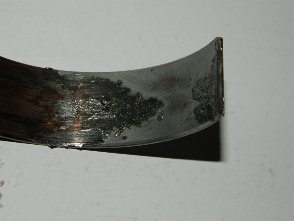 Worn engine bearing with dark deposits and scoring