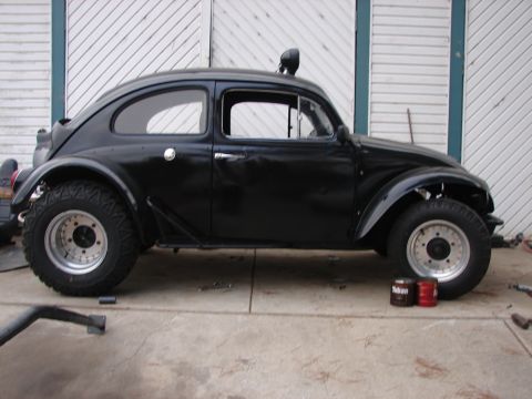 1964 Volkswagen Beetle - A modified black Volkswagen Beetle sits parked in front of a garage door, equipped with off-road tires.