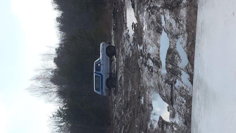 White and blue SUV driving through a muddy, wet terrain with trees in the background