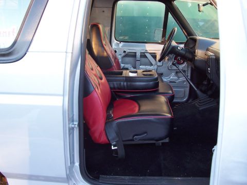 1990 Ford Bronco - The interior of a truck features custom seats with red and black flame upholstery and a prominent center console with cup holders.