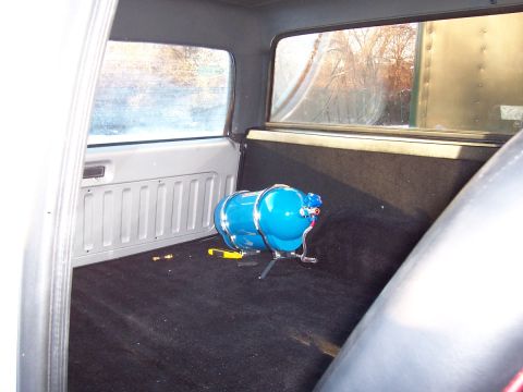 1990 Ford Bronco - The interior of a vehicle shows a blue nitrous oxide tank and a yellow tool on the carpeted floor.