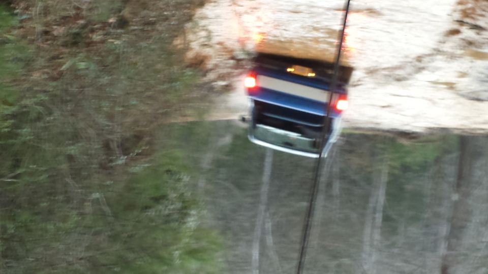Blue SUV with a white stripe on the tailgate driving through muddy water, rear view