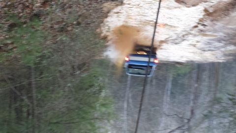 1979 Ford Bronco - A blue SUV is being winched up a steep, muddy hill through a wooded area.