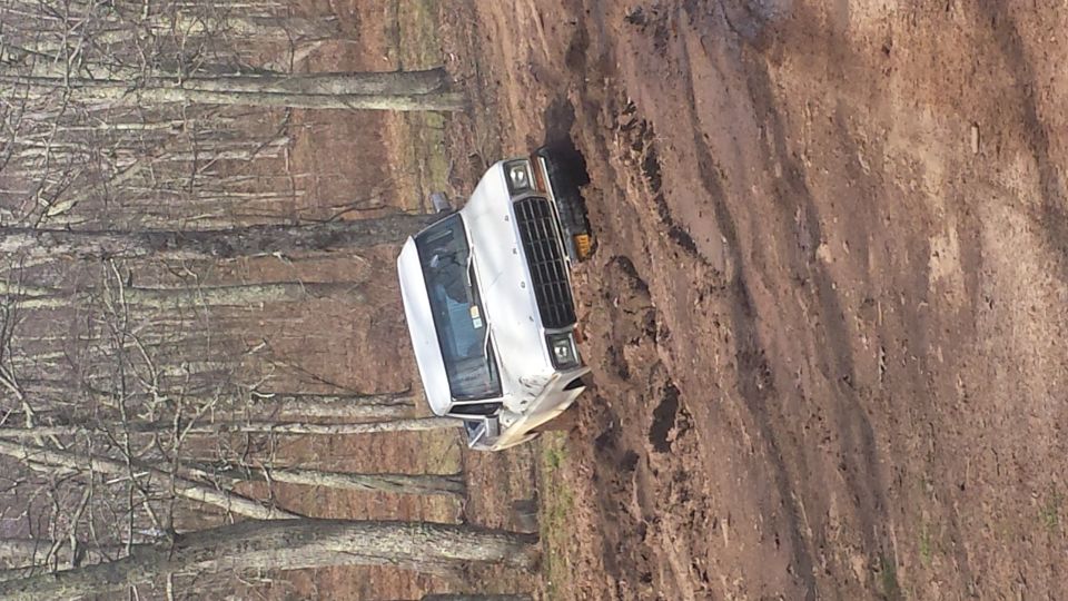 White SUV tilted on a muddy incline with trees in the background