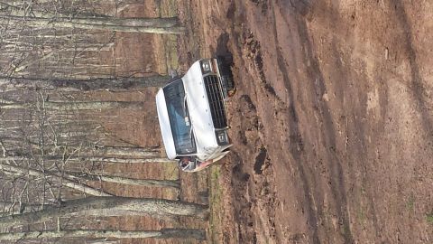 1979 Ford Bronco - A white SUV navigates a steep, muddy trail through a wooded area.