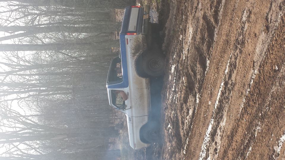 White and blue pickup truck driving through mud and trees