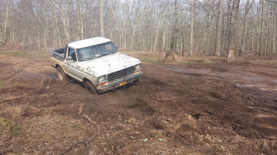 White pickup truck stuck in deep mud on a wooded trail