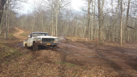 1979 Ford Bronco - A white pickup truck is stuck in the mud on a winding dirt road through a forest.
