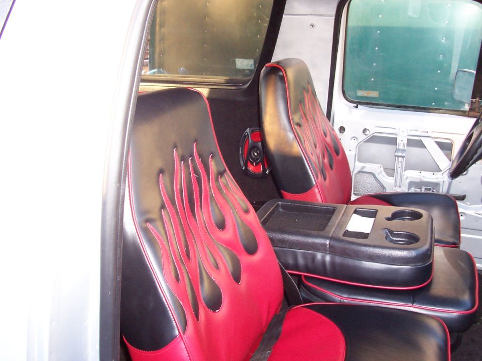Seats with red flames on black upholstery, center console with cup holders, and speakers visible inside a vehicle