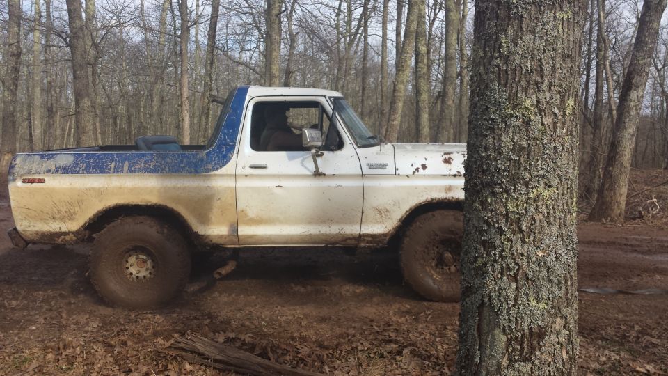 White and blue Ford Bronco with large tires on a muddy trail
