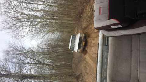 1979 Ford Bronco - A white van navigates a muddy trail surrounded by bare trees.