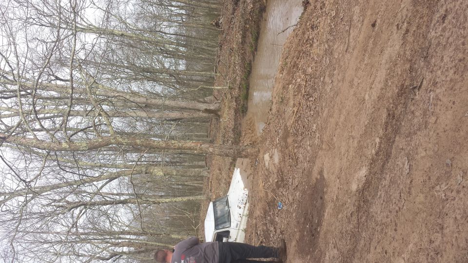 White SUV stuck in a muddy ditch with trees in background