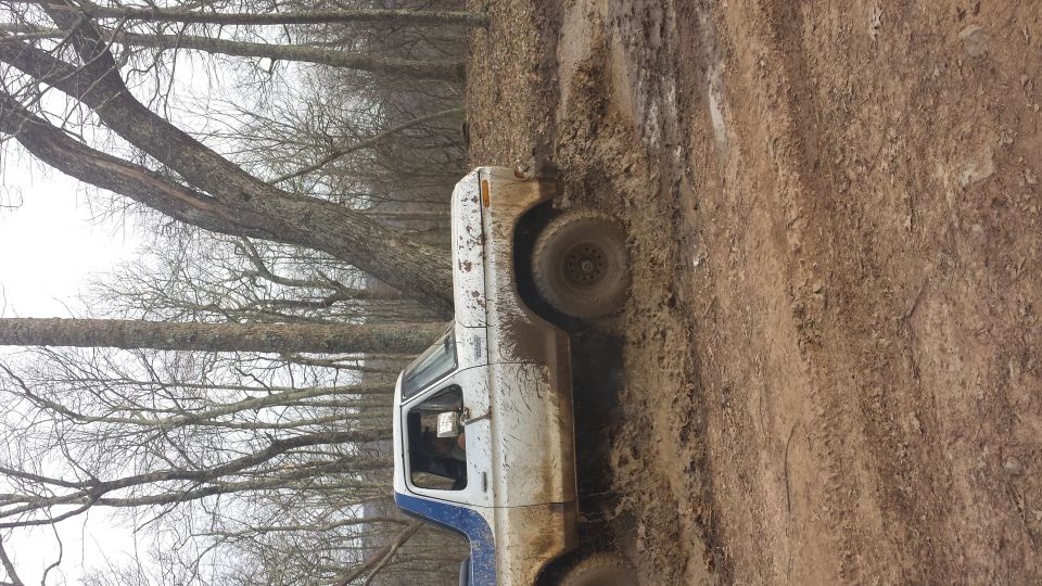 1979 Ford Bronco side view, white and blue, stuck in mud on wooded trail
