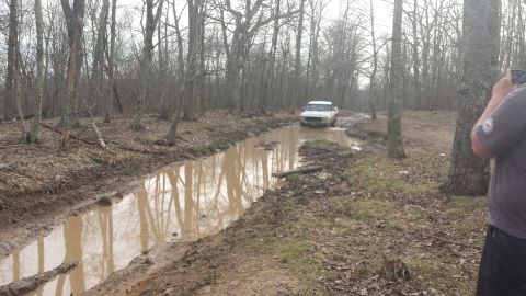 1979 Ford Bronco - White 1979 Ford Bronco navigating a water-filled dirt path in a forest.