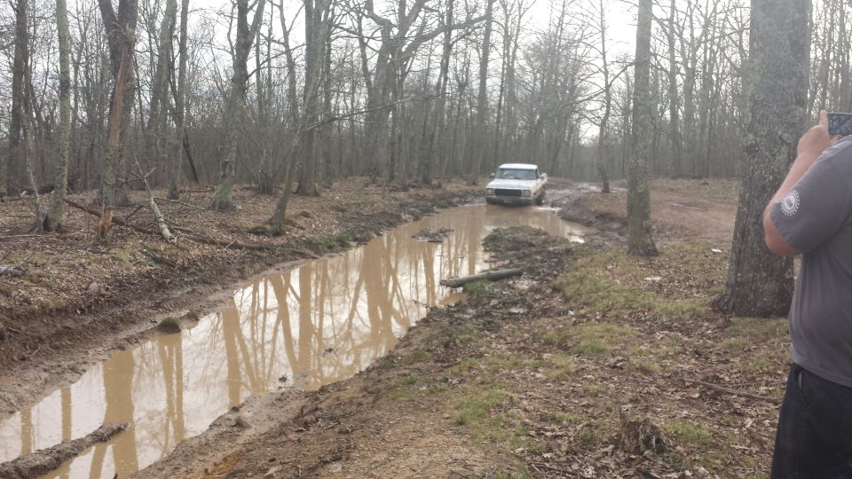 1979 Ford Bronco driving through a muddy trail in a wooded area
