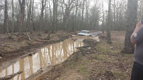 1979 Ford Bronco - A white 1978 Ford Bronco navigates a challenging mud pit in a wooded area.