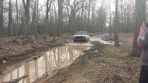 1979 Ford Bronco - Off-road vehicle navigates a challenging muddy path in a wooded area.