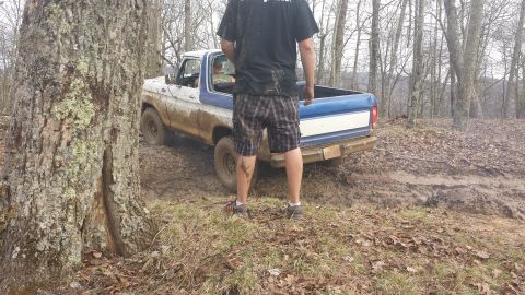 1979 Ford Bronco - A blue and white Ford Bronco navigates a muddy trail in a wooded area.