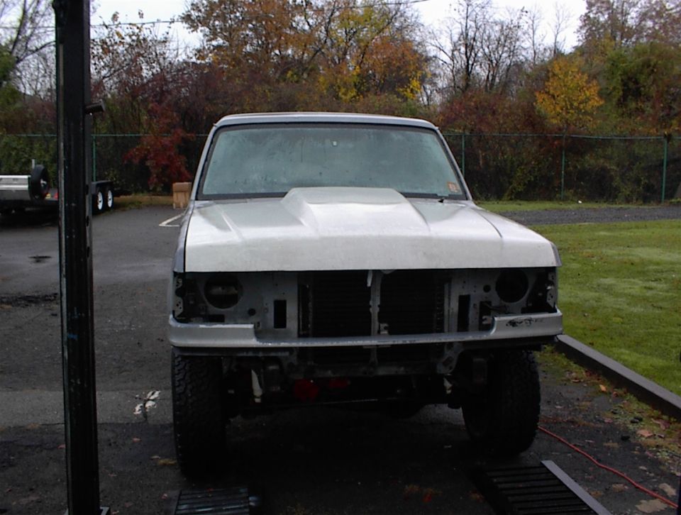 Front view of a white truck with an aftermarket hood and missing headlights