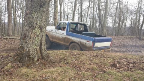 1979 Ford Bronco - A muddy white and blue Ford Bronco navigates a challenging off-road trail.