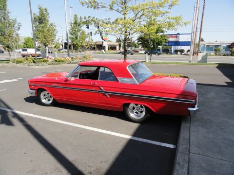 1964 Ford Fairlane - This red 1964 Ford Fairlane coupe is parked in a lot, showing its distinctive body style and chrome trim.