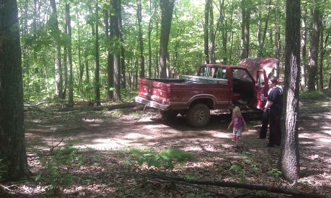 1979 Ford Bronco - Red pickup truck in woods with hood open. Two adults and a child are present.