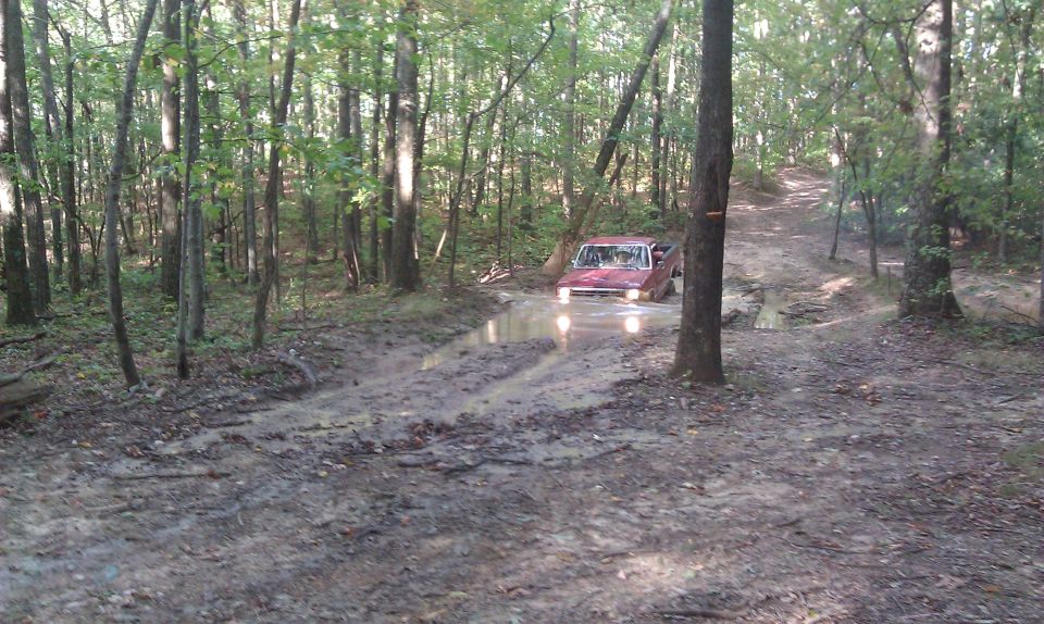 Red pickup truck navigating a muddy trail in a forest