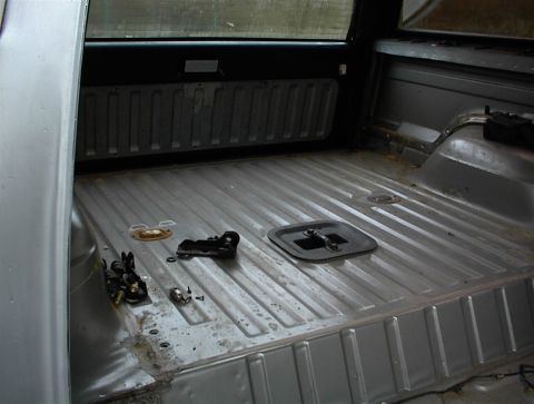 1990 Ford Bronco - The interior of a truck bed is shown, stripped down with various parts scattered on the floor.