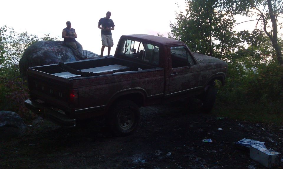 Red pickup truck, weathered, parked on dirt with two men nearby