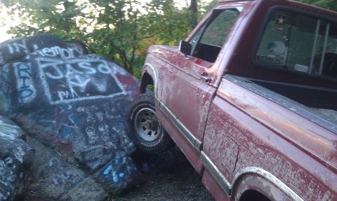 1979 Ford Bronco - A red pickup truck is positioned next to large rocks covered in graffiti.