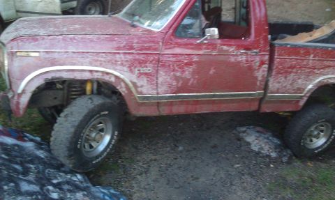 1979 Ford Bronco - Mud-covered red pickup truck, possibly a 1979 Ford F-150, with lifted suspension and off-road tires.
