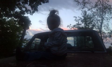 1979 Ford Bronco - A child sits on the hood of a truck as the sun sets, silhouetted against the colorful sky.