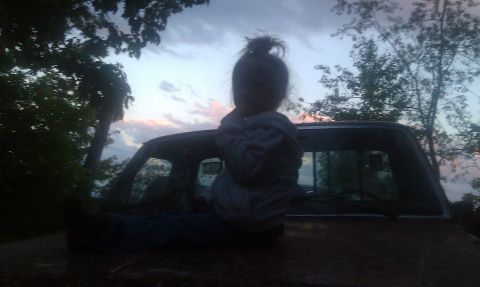 1979 Ford Bronco - Child sits on the hood of a pickup truck as the sun sets.