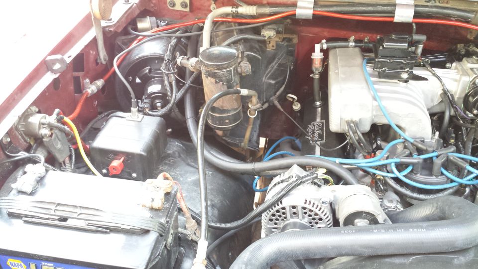 Engine bay of a 1992 Ford Bronco with Edelbrock intake, blue plug wires, alternator, and NAPA battery