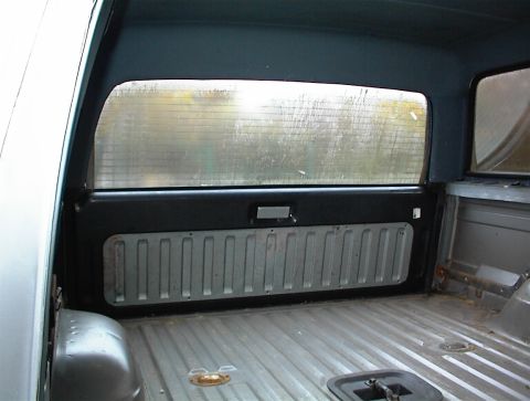 1990 Ford Bronco - The interior of a truck bed is visible, ribbed flooring and side paneling, with a view through the rear window.