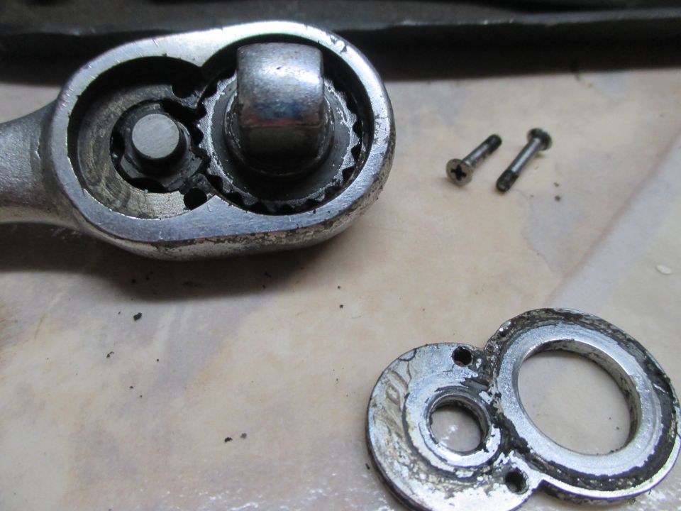 Disassembled ratchet wrench mechanism with two screws and a circular plate